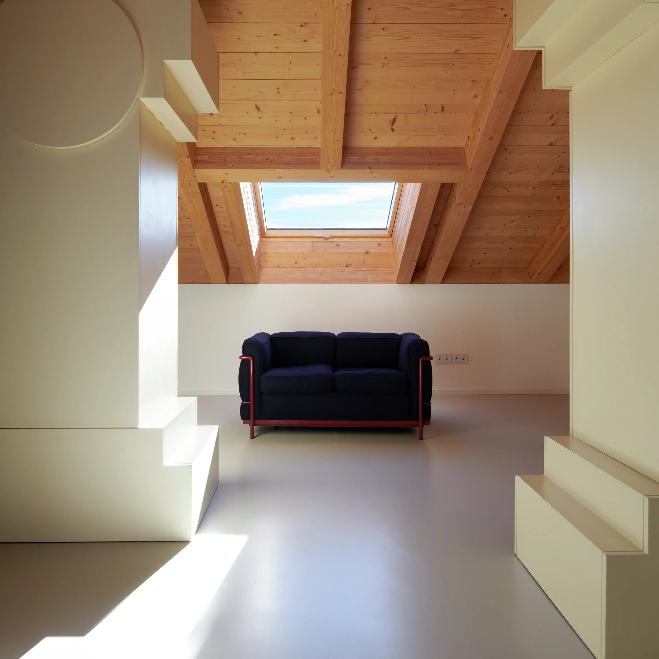 Une pièce lumineuse et aérée avec un plafond en bois, des murs blancs et un canapé noir, éclairée par une fenêtre de toit Velux.